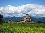 Uzaktan kilise, önde tarla, arkada tepeler