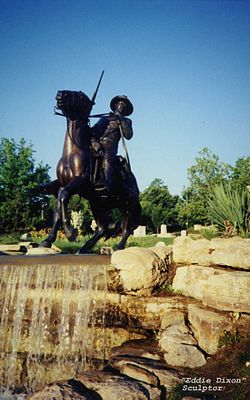 Uma fotografia colorida do Monumento ao Soldado Buffalo em Fort Leavenworth, Kansas.  A escultura foi realizada por Eddie Dixon e fica no topo de uma cachoeira.  Consiste em um soldado de cavalaria montado em um cavalo a galope