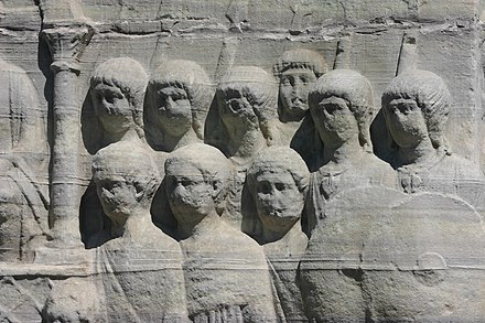 Late Roman soldiers, probably barbarians, as depicted (back row) by bas-relief on the base of Theodosius I's obelisk in Constantinople (c. 390). The troops belong to a regiment of palatini as they are here detailed to guard the emperor (left). More than third of soldiers in the palatini were barbarian-born by this time. Note the necklaces with regimental pendants and the long hair, a style imported by barbarian recruits, in contrast to the short hair that was the norm in the Principate