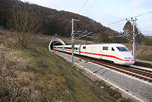 Weißer elektrischer Zug mit roter Cheatline, die aus dem Tunnel auf dem Lande auftaucht