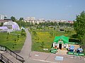 English: View of Victory Park from Red Army bridge. The red brick building on the left is Lyceum no.1; in front of it is a bandstand; on the right is a summer cafe; also a few tanks, a rocket and many dandelions. Русский: Вид на Парк Победы с Красноармейского моста. Кирпичное здание слева — Лецей №1; перед ней — эстрада для оркестра; справа — летнее кафе; дальше несколько танков, одна ракета и очень много одуванчиков