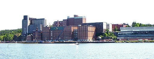 Kvarnholmens östra del, vy från Södra Djurgården över Stockholms inlopp, med Kvarnen Tre Kronor och silobyggnaden i färdigt skick på 1930-talet (vänster bild), samma vy i juni 2010 med kontorshuset "Munspelet" längst till höger.