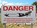 Tanda peringatan, berdiri terlalu dekat dengan pagar bandar udara di Pantai Maho dapat berbahaya.