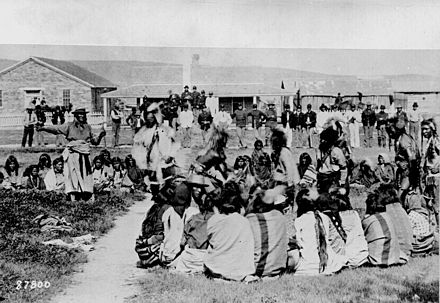 "Shoshone at Ft. Washakie, Wyoming Native American reservation. Chief Washakie (at left) extends his right arm." Some of the Shoshones are dancing as the soldiers look on, 1892.