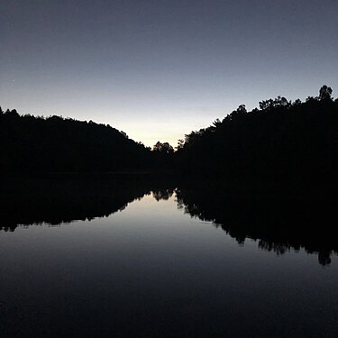 The reflection of the far shore/tree line of a lake at sunset