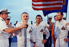 Quatre personnes en uniforme blanc en dessous d'un drapeau américain.