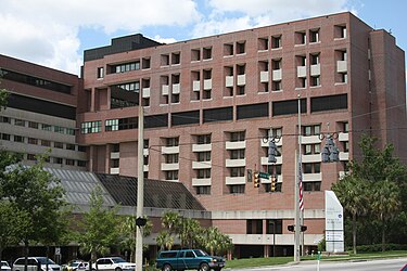 На фотографии изображено одно крыло Медицинского научного центра Дж. Хиллиса Миллера, современного комплекса из красного кирпича, который включает в себя учебную больницу Университета Флориды и медицинские, медсестринские, стоматологические и фармацевтические колледжи.
