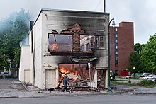 MetroPCS store with apartment units above on fire in Minneapolis, May 28, 2020. A man walks by a burning building on Thursday morning after a night of protests and rioting in Minneapolis, Minnesota (49945327763).jpg