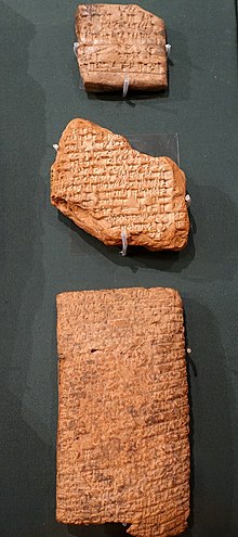 Trois tablettes d'argile accrochées à un mur. Elles sont alignées verticalement et recouvertes de caractères cunéiformes.