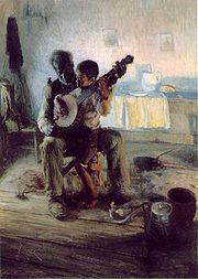 A boy holding a banjo seated on an old man's lap