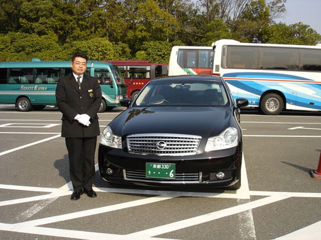 A chauffeur in Japan standing next to a Nissan Fuga