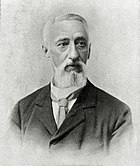 A grey-haired man with a dark jacket and a tie