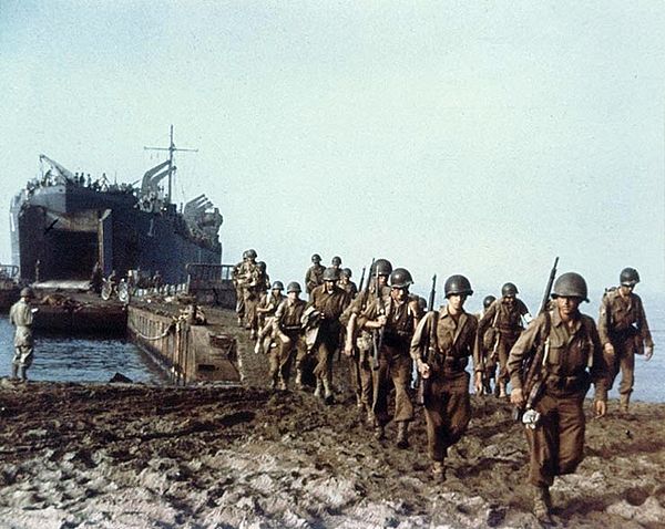 A U.S. Navy Landing Ship, Tank (LST-1) landing American Army troops possibly from the 36th Division on an Italian beach, via a causeway