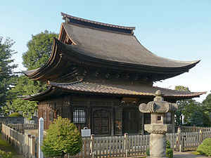 Tall wooden building with a hip-and-gable roof and a pent roof on all sides in the lower part.
