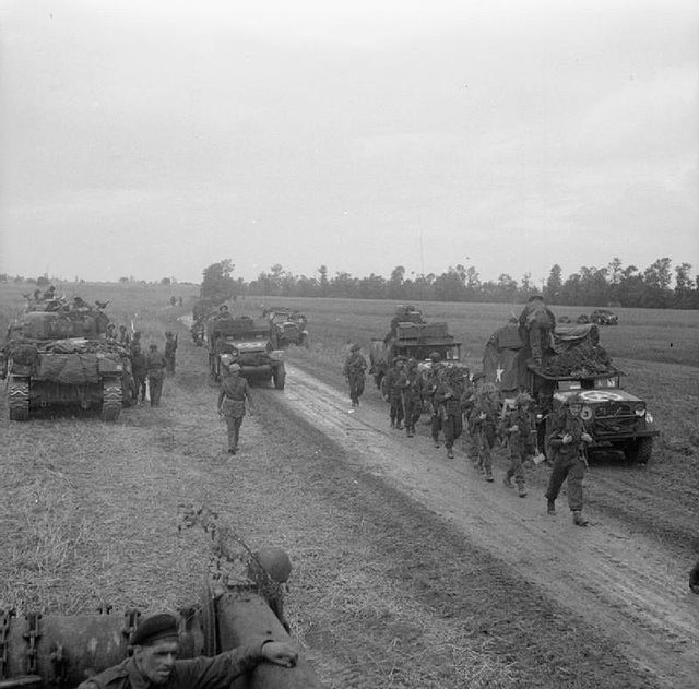 Men of the 10th Battalion, Highland Light Infantry advance past vehicles of 15th (Scottish) Division during Operation 'Epsom', 26 June 1944. On the le