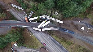 Aerial view of the wreckage after the derailment, showing train cars on the bridge and the freeway below.
