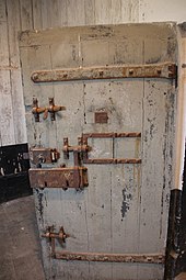 Fotografia a colori di una robusta porta in legno con più serrature e chiavistelli.