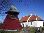 Ännu en panelklädd täckt klockstapel vid Bergums kyrka utanför Göteborg. Den lutande formen avslöjar att grundstrukturen också här är en bock.