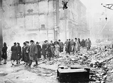 Office workers make their way to work through debris after a heavy air raid.