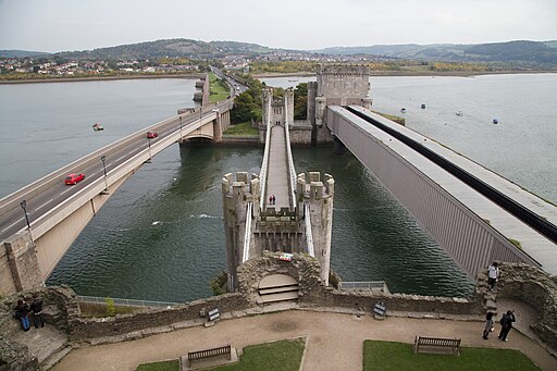 Conwy. Blick von Conwy Castle nordostwärts. In der Mitte die Conwy Suspension Bridge, rechts die Conwy Railway Bridge. Im Vordergrund drei Türme von Conwy Castle (UNESCO-Welterbe in Wales)