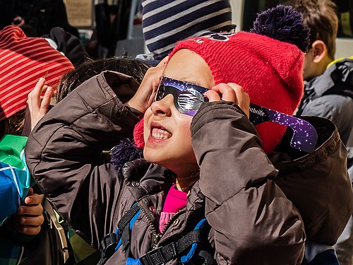 Child protecting his eyes against the sunlight with special cardboard sunglasses during the solar eclipse on March 20th 2015