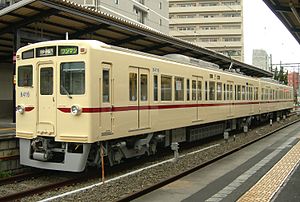 Ivory-white commuter train with dark red bodyside stripe