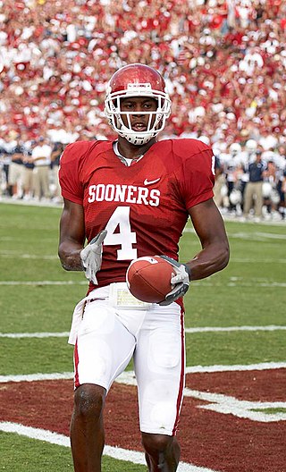 An American football player wearing a red helmet, red jersey (number 4) and white pants holds a football after scoring a touchdown in a game.