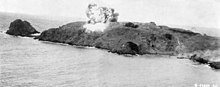 Photographie aérienne en noir et blanc d'une île longiligne avec une boule de feu en son centre.