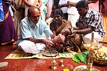 A baby's paternal grandfather in Kerala performing Nool Kettu by tying a black string on the waist of the child NoolKettu.JPG