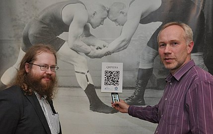 Il direttore del Museo dello sport estone che inquadra un codice QRpedia, a fianco un esponente di Wikimedia Estonia.