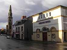 The Theatre Royal in Dumfries. In the background can be seen the spire of the old St Andrew's Cathedral: the rest of the building burned down in 1961[37] and was replaced with a new church on the same site.