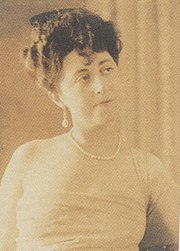 Photographie sépia d'une femme en buste, cheveux en chignon 1900, épaules dénudées et collier de perles.