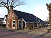 Woning met zesruitsvensters en kleine topvensters onder breed zadeldak met topschoorsteen met bord en stal in het verlengde van de woning