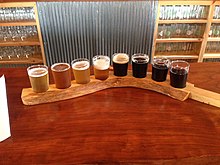 A flight of eight beers, served on a curved beer stick, arranged in order from light to dark, at a bar in West Virginia, United States Big Timber Brewing flight of beer.jpg