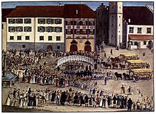 Peinture montrant une fête sur une grande place avec des chariots remplis de céréales.