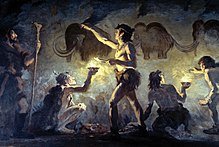 Peinture représentant quatre hommes préhistoriques, dont trois assis, représentant des mammouths en peignant avec leurs doigts sur les parois d'une grotte. Un cinquième homme se tient debout à côté avec un bâton dans la main.