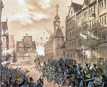 Dans la ville, un grand groupe de cavaliers en uniforme bleu se dirige au galop vers les barricades au fond.