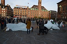 Twelve large blocks of ice cast off from the Greenland ice sheet are harvested from a fjord outside Nuuk and presented in a clock formation in Copenhagen in 2014. The work raises awareness of climate change by providing a direct and tangible experience of the reality of melting arctic ice. Ice Watch (37898431101).jpg