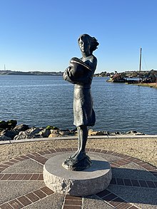 Bronze statue of a woman holding a pelican. Behind the statue is the ocean.