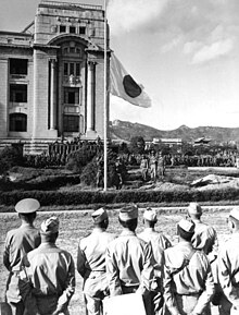 Männer in Militärkleidung beobachten, wie eine Flagge gesenkt wird.