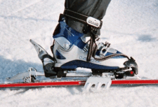 Alpine touring ski boot, binding, and ski crampon. The red spot below the toe portion is the pivot point of the binding about which the rest of the boot turns during a step, resulting in a movement similar, but not identical to a normal human walking movement - the shoe tip is always at the same height, because the skis are moved to glide at the snow surface level. TouringBinding1.gif