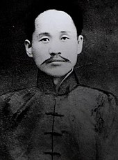 Fotografie alb-negru care prezintă un bărbat cu mustață și în haine tradiționale din față.