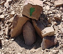 Trois pierres plates dressées sur un sol caillouteux et surmontées d'une pierre carrée marquée à la peinture verte.