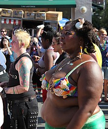 Femme noire en bikini arc-en-ciel, lors d'une gay pride, sous le soleil.