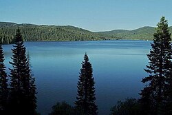 Большое озеро под голубым небом, окруженное лесными холмами с крутыми склонами под чистым голубым небом.