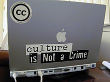 An Apple laptop computer decorated with Creative Commons stickers and the phrase "culture is not a crime." A small black and white CC sticker is placed on the upper left back of the computer that reads "Creative Commons. Some Rights Reserved."