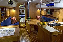 Cruising yacht interior with fold-down table in main salon, galley (kitchen) on right, and navigation station on left and forward cabin visible beyond. J133interior.jpg