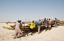 Port de Pêche. Die Boote mit Außenbordmotoren werden über Rollen aus dem Wasser gezogen, die Fische in Holzkisten auf Eselkarren zur Auktionshalle im Hintergrund gebracht