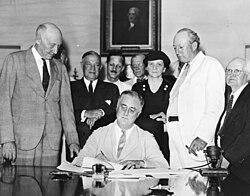 President Roosevelt signs the Social Security Act, at approximately 3:30pm ET on August 14, 1935. Standing with Roosevelt are Rep. Robert Doughton (D-NC); unknown person in shadow; Sen. Robert Wagner (D-NY); Rep. John Dingell Sr. (D-MI); unknown man in bowtie; Secretary of Labor, Frances Perkins; Sen. Pat Harrison (D-MS); and Rep. David Lewis (D-MD). Signing Of The Social Security Act.jpg