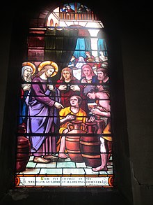 Vitrail représentant Jésus auréolé pointant son doigt vers des tonneaux, entouré d'une petite foule de personnages secondaires.